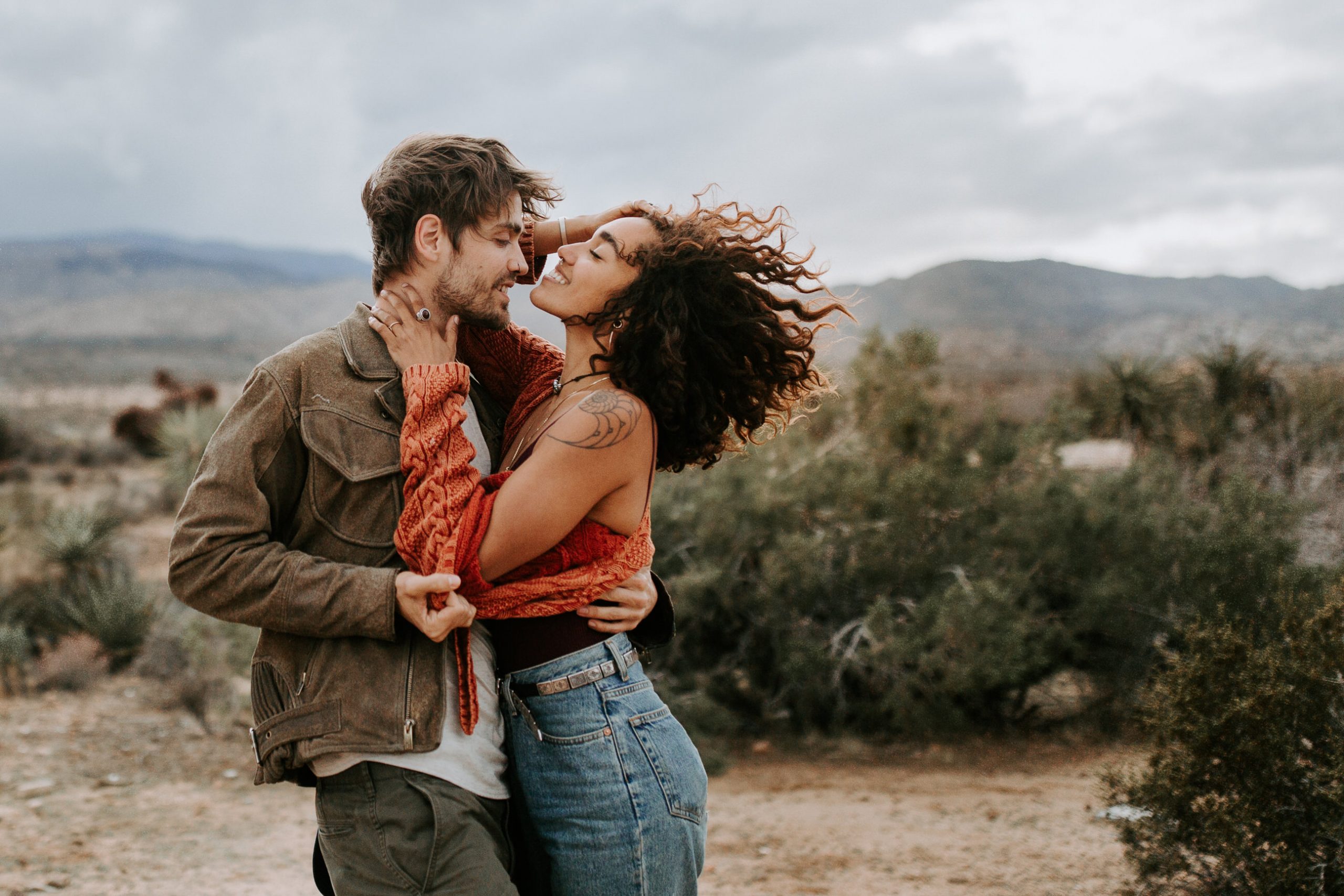 Couple with wind blown hair and tattoos laughing in Joshua Tree California 