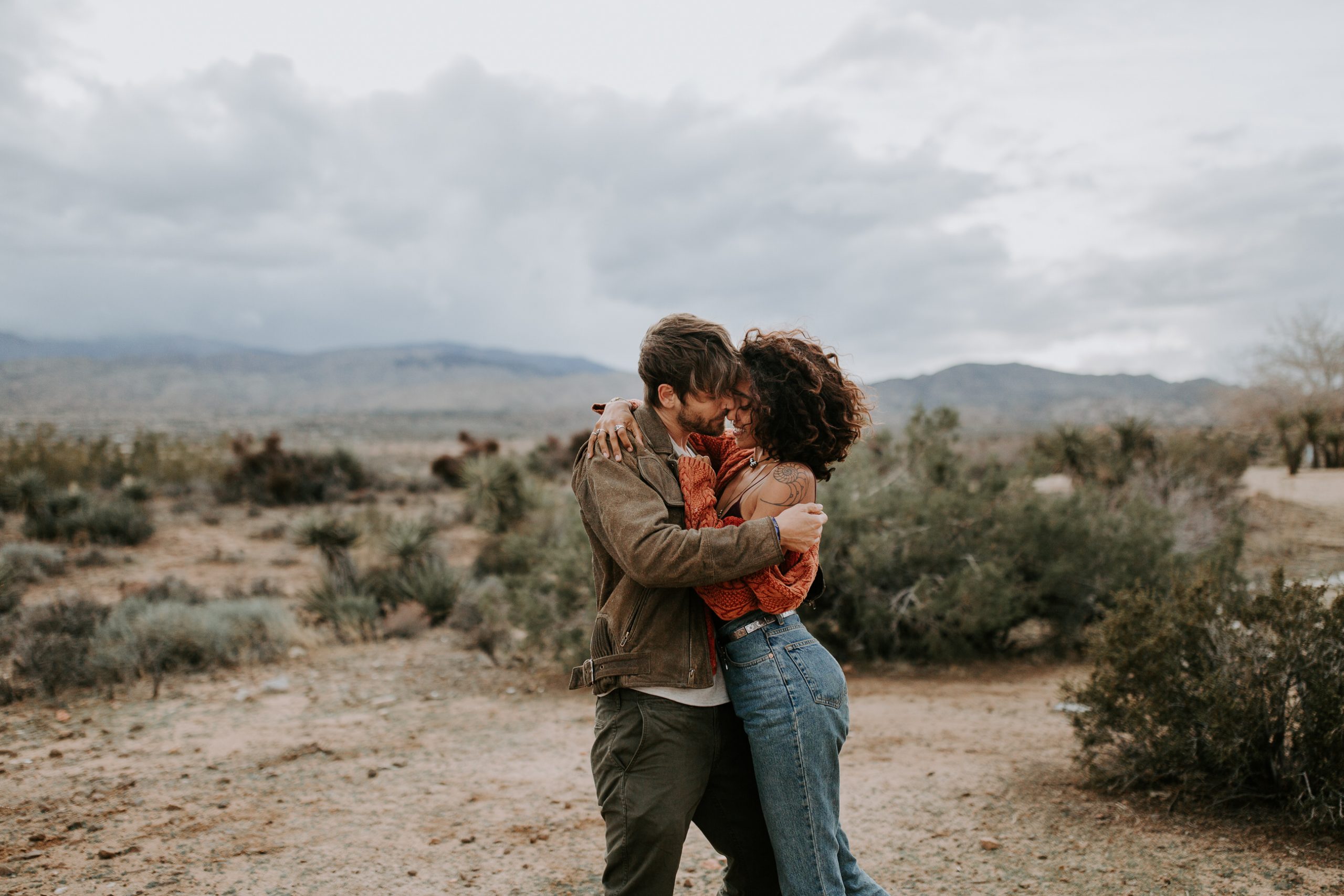 Couple with wind blown hair and tattoos laughing in Joshua Tree California 
