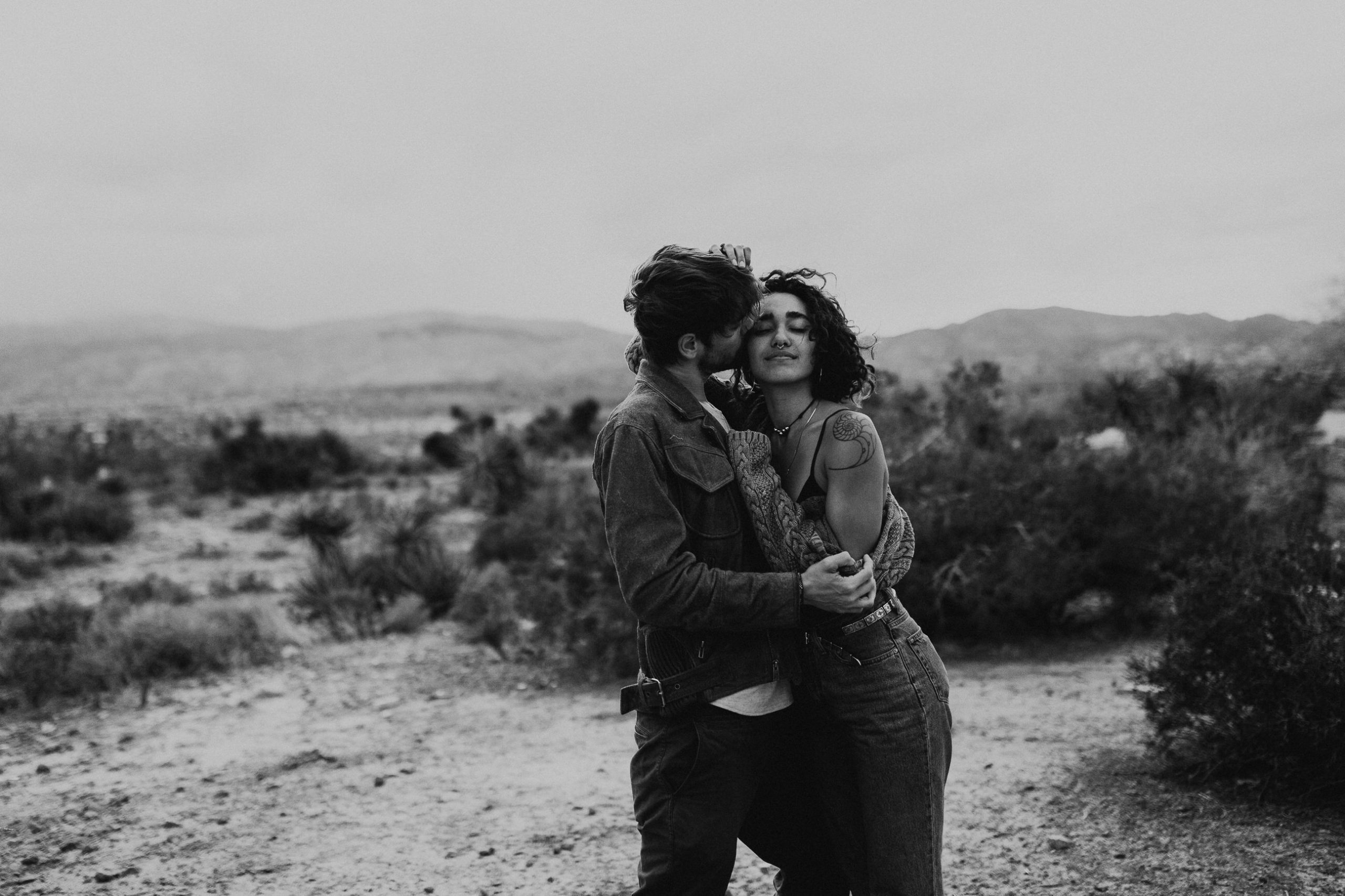 Couple with wind blown hair and tattoos laughing in Joshua Tree California