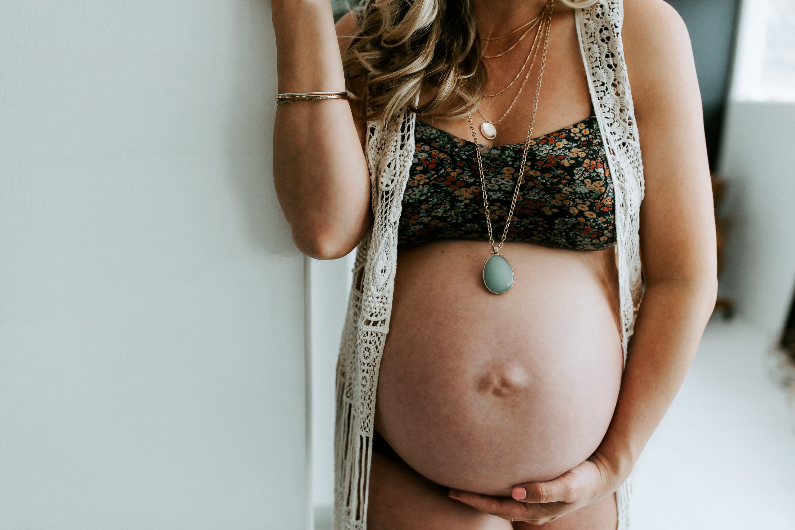 Boho Inspired Maternity Session - woman on white wall holding belly 