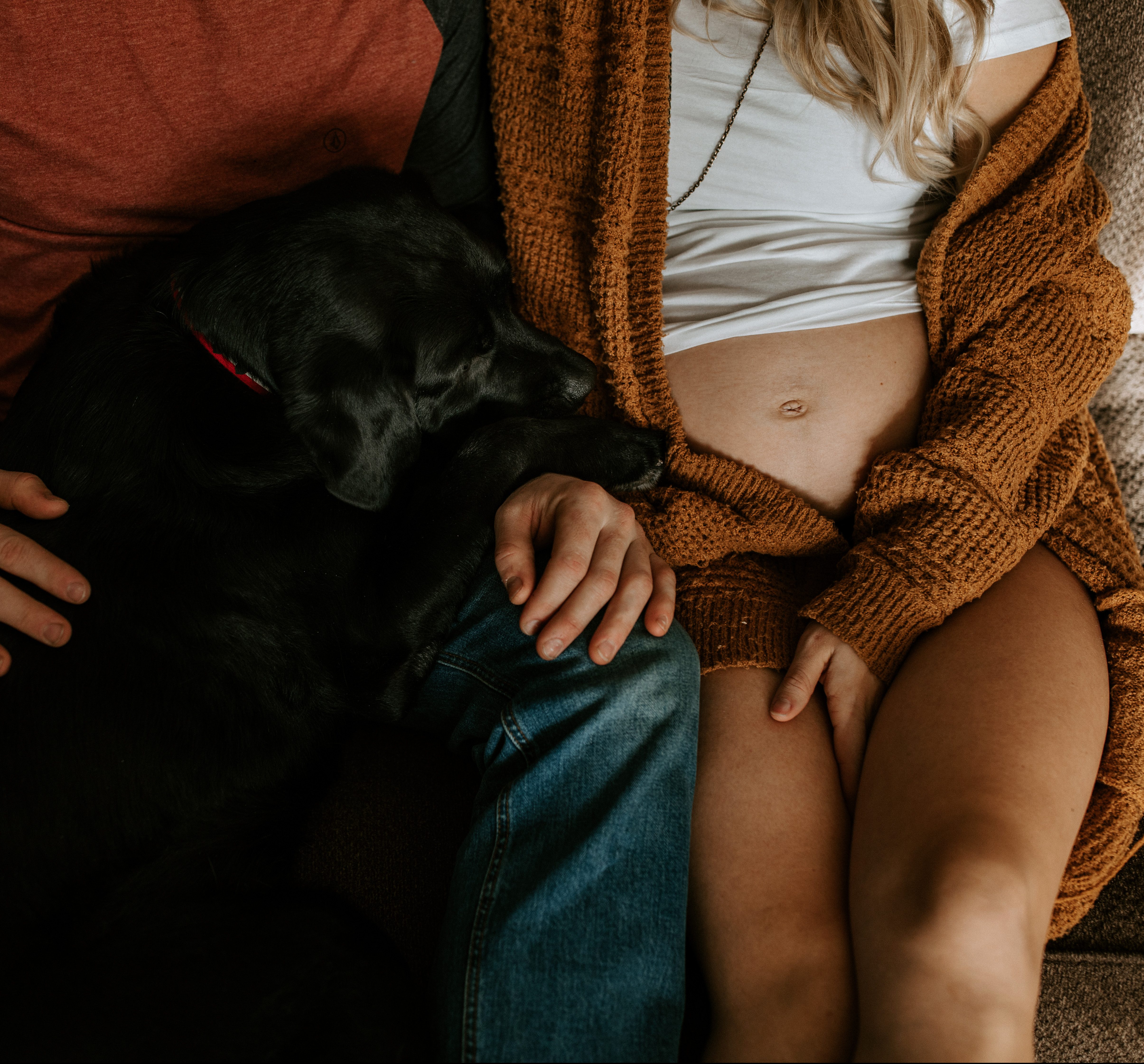 cute pregnant couple with their black lab sitting on a couch cuddling