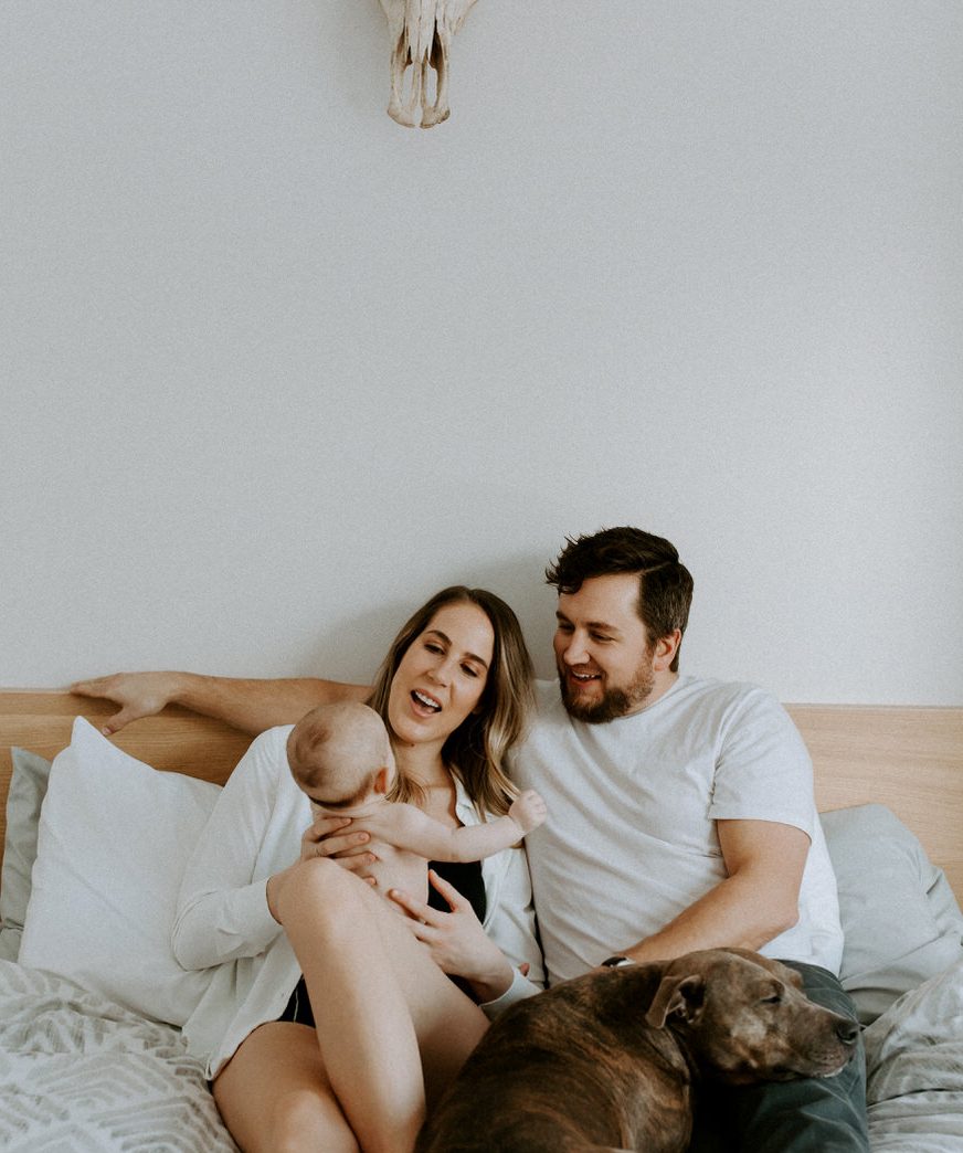 family cuddle up in bed with their newborn at home and their dog